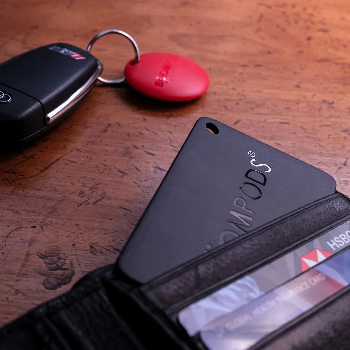 Black wallet tracker with GPS attached to keys and placed inside a black leather wallet on wooden surface