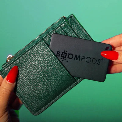 Wallet tracker with GPS being placed into a green leather cardholder wallet by a hand with red nails