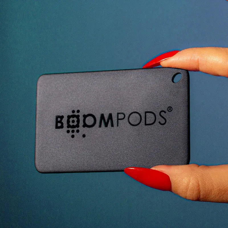 Black BOOMPODS wallet tracker with GPS device held between fingers with red nails